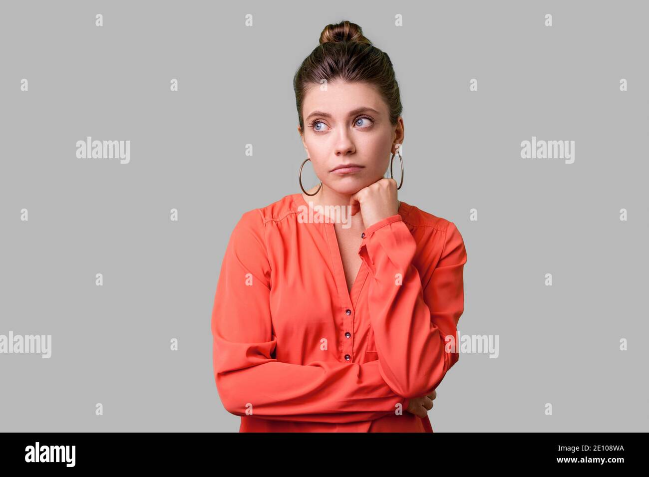 Portrait de femme élégante de ressentiment avec bun hairstyle, big earrings et en blouse rouge à côté, tenant son menton et méditant tristement, déprimé. Banque D'Images