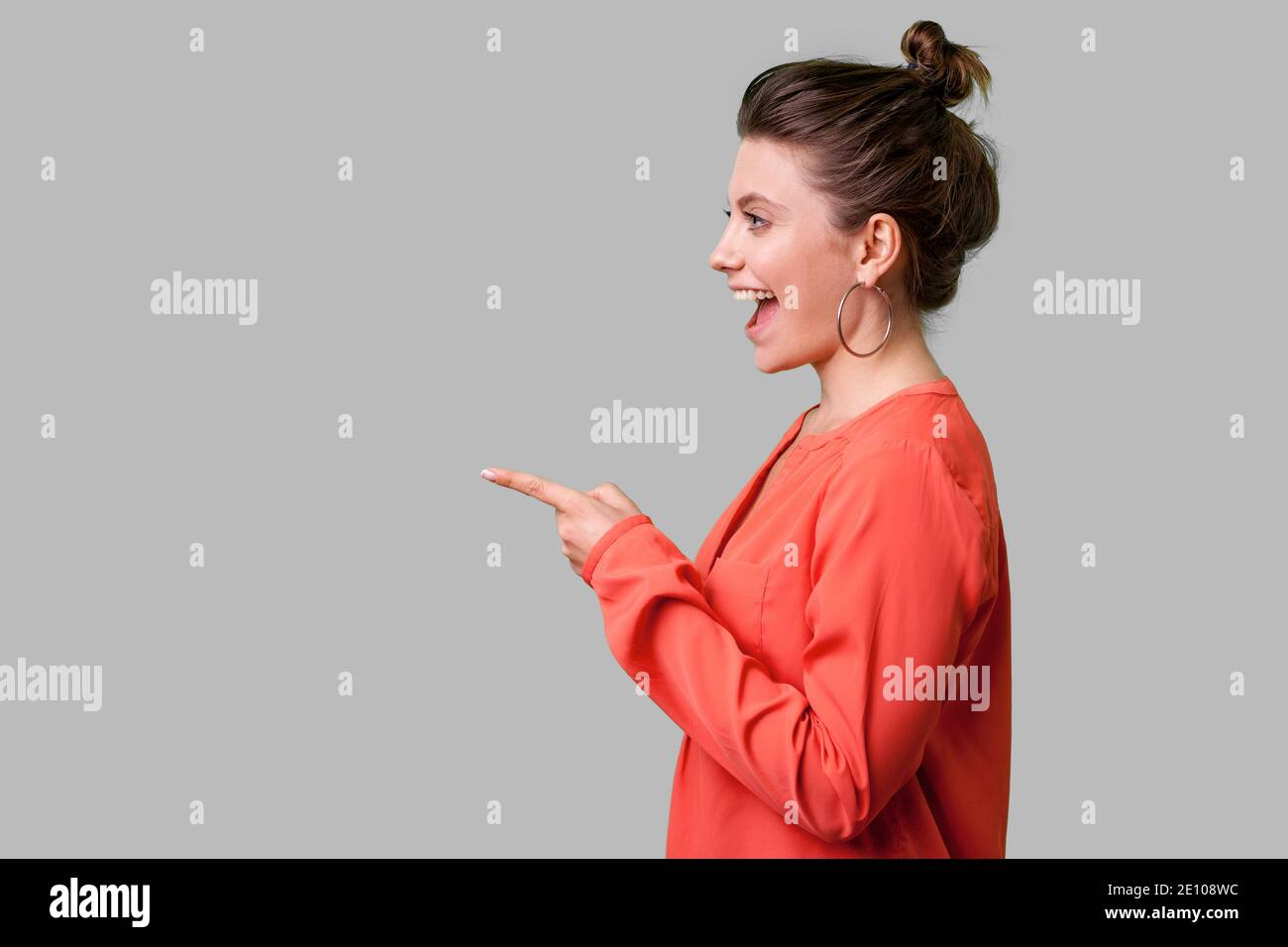 Hey you ! Vue de côté portrait de surpris fille avec bun hairstyle, big earrings et en rouge blouse doigt vers la gauche, à la recherche d'étonnement. Banque D'Images