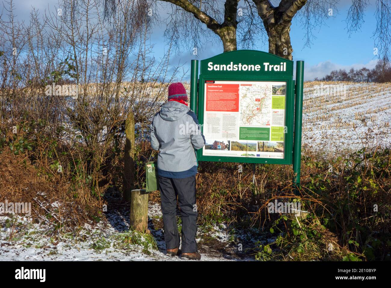 Une femme s'est arrêtée pour lire le tableau d'information sur Coppermine Lane La marche de la piste de grès Cheshire un long chemin de pied dans hiver après la neige Banque D'Images