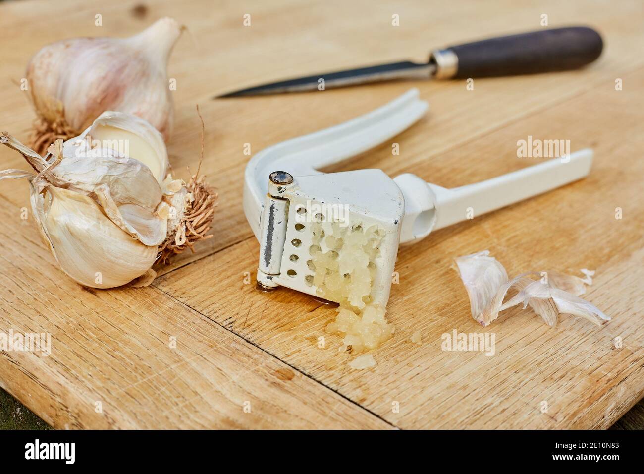 Bulbes à l'ail, couteau et presse sur la planche à découper avec de l'ail fraîchement pressé, vue horizontale 2 Banque D'Images