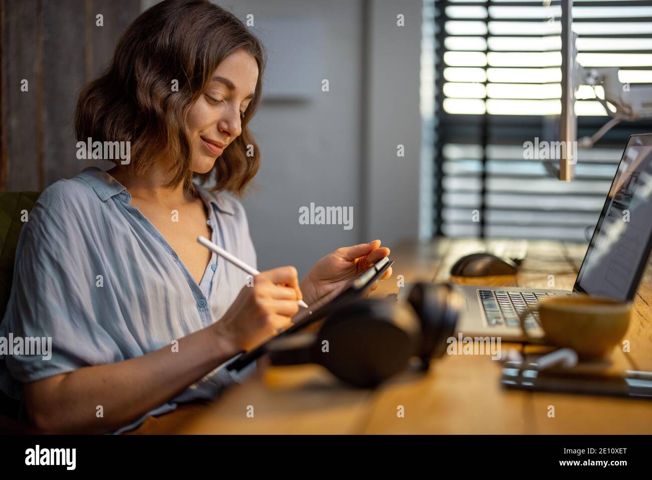 Jeune femme vêtue à la manière décontractée ayant un peu de travail créatif, dessin sur une tablette numérique, assis dans le bureau à la maison confortable et élégant Banque D'Images