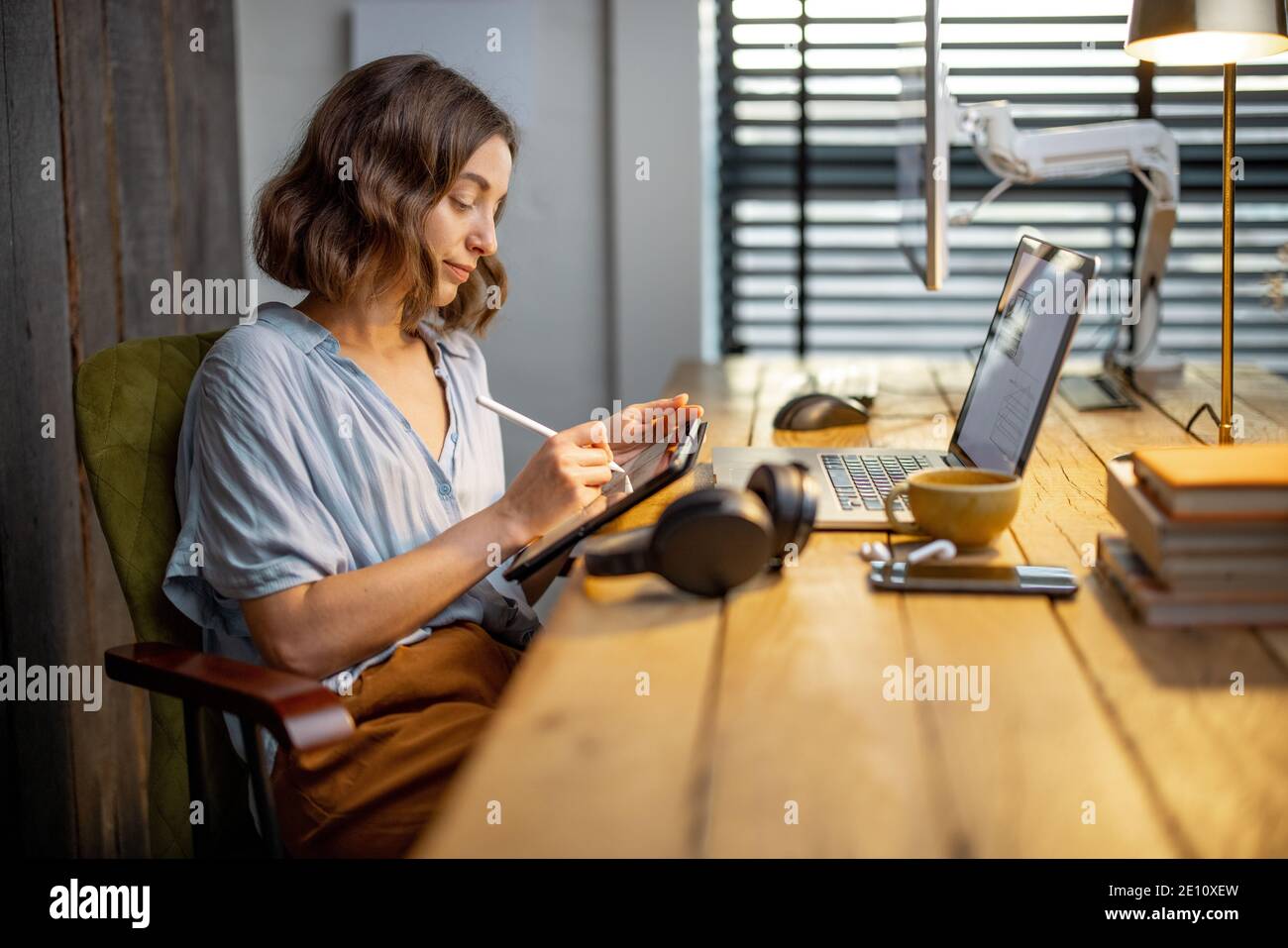 Jeune femme vêtue à la manière décontractée ayant un peu de travail créatif, dessin sur une tablette numérique, assis dans le bureau à la maison confortable et élégant Banque D'Images