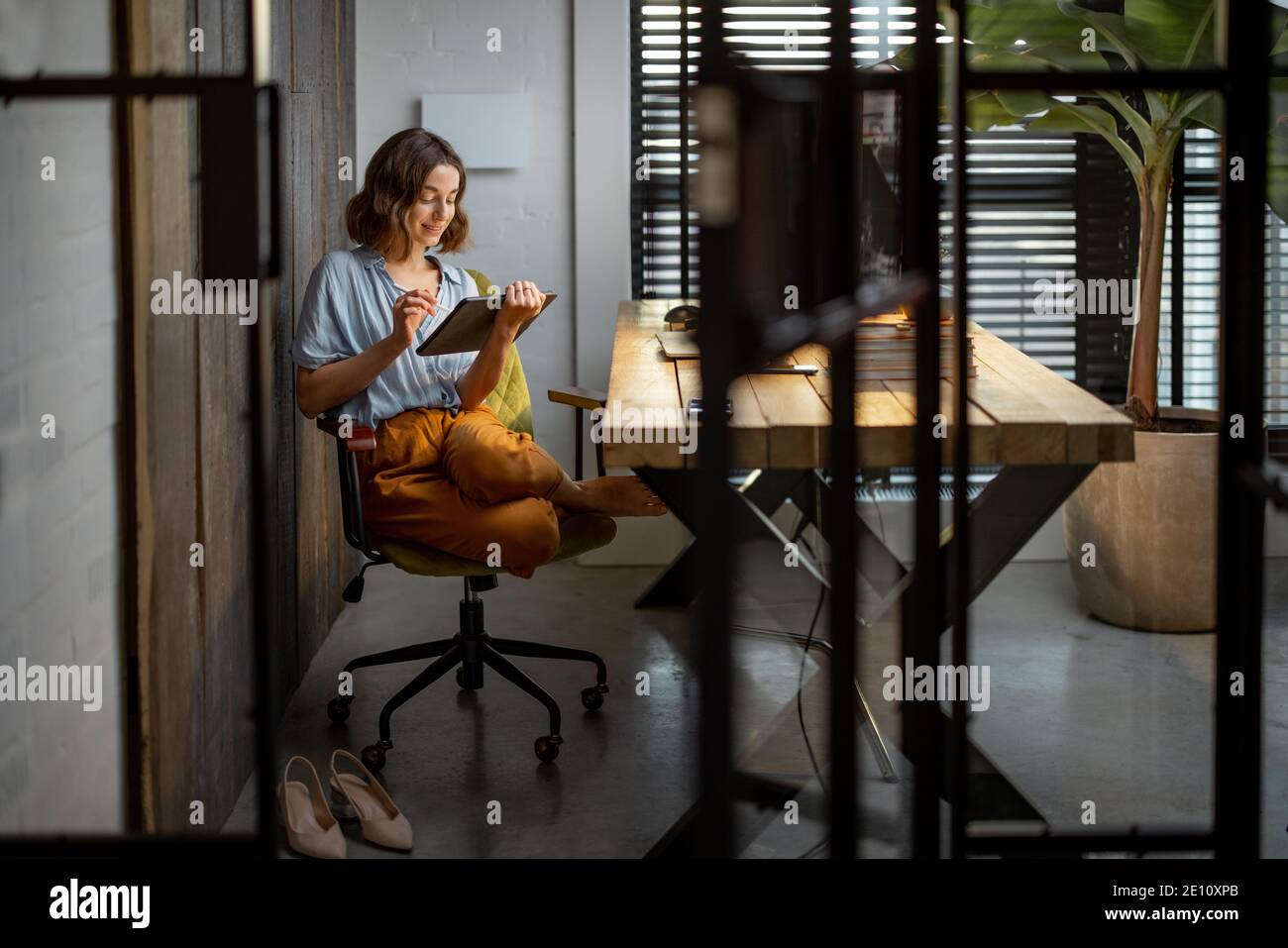 Femme créative travaillant sur un pavé tactile dans le bureau à domicile confortable et élégant. Prise de vue complète Banque D'Images