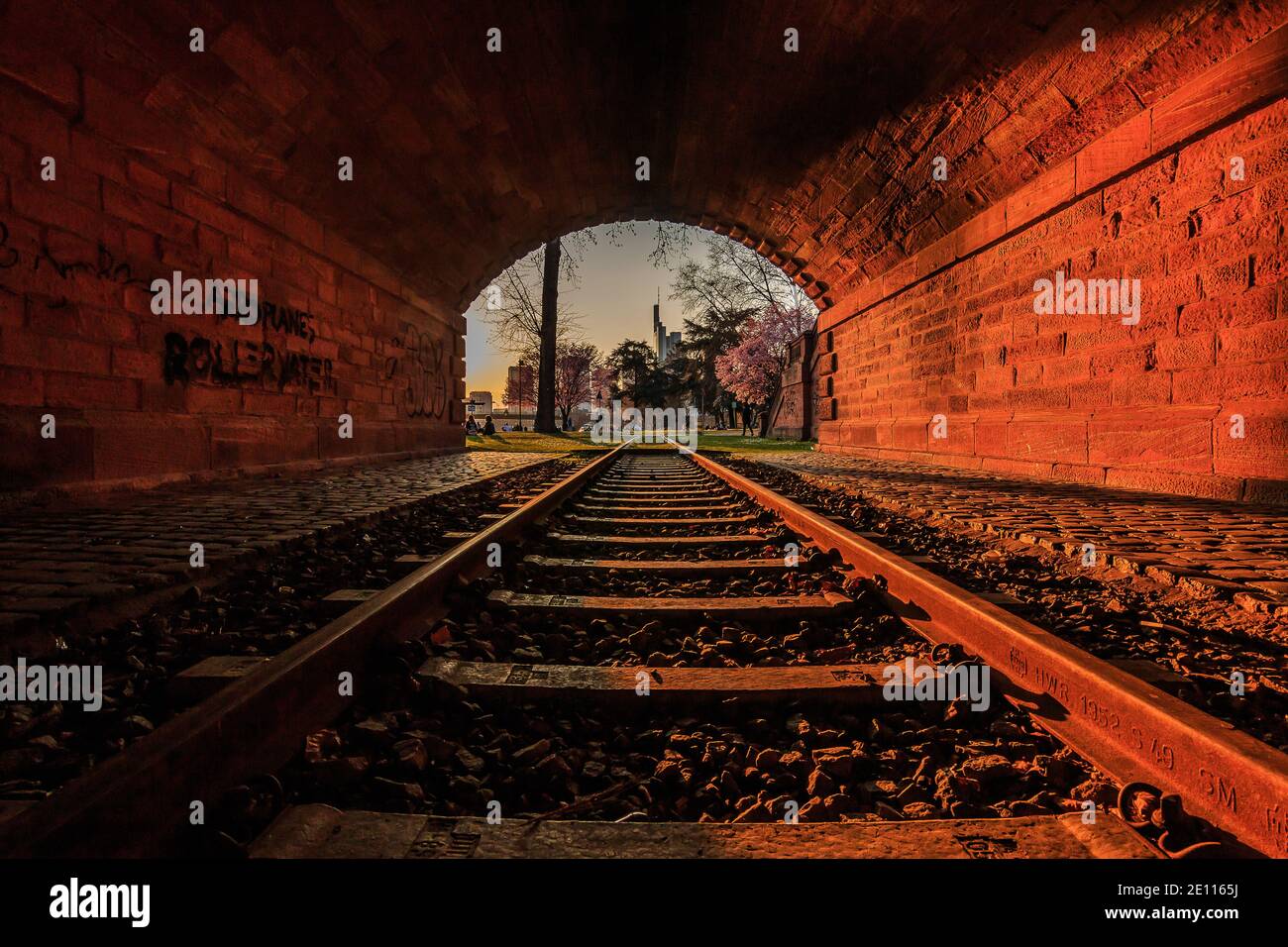 Vieux tunnel avec chemin de fer dans la soirée au coucher du soleil. Horizon de Francfort à la sortie du tunnel. Parc avec arbres et prairie au printemps avec fleurs Banque D'Images