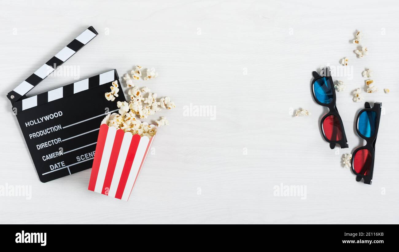 Clapperboard de cinéma, lunettes 3d colorées et seau à rayures rouges avec pop-corn sur fond de bois blanc, vue du dessus. Arrière-plan du cinéma. Banque D'Images