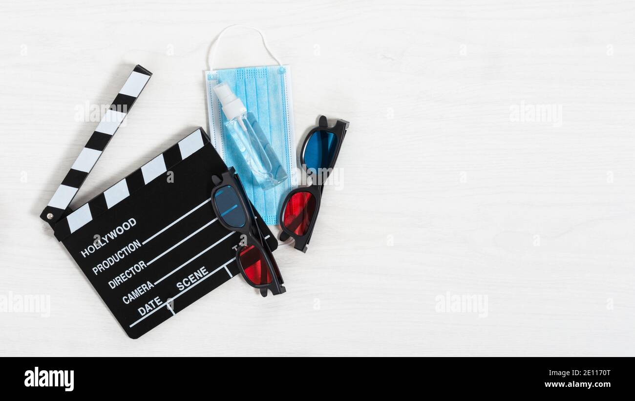 Clapperboard de cinéma, lunettes 3D colorées, masque de protection contre les virus et désinfectant pour les mains sur fond de bois blanc. Cinéma en temps de pandémie concept. Banque D'Images