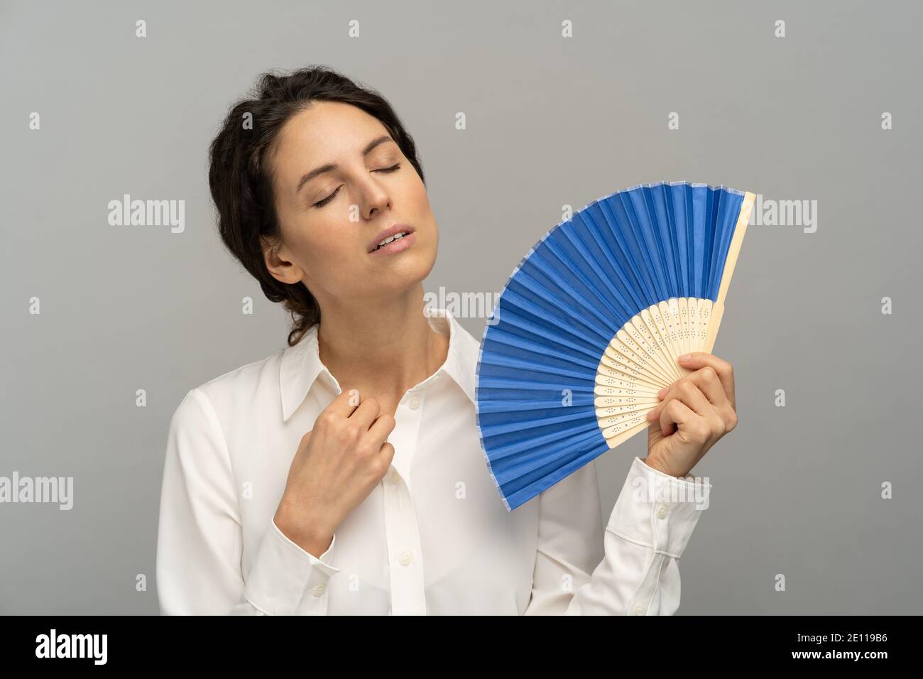 Une femme fatiguée surchauffée, un employé, détouche le bouton supérieur du chemisier, utilisant un ventilateur à vagues souffrent de transpiration de chaleur Banque D'Images