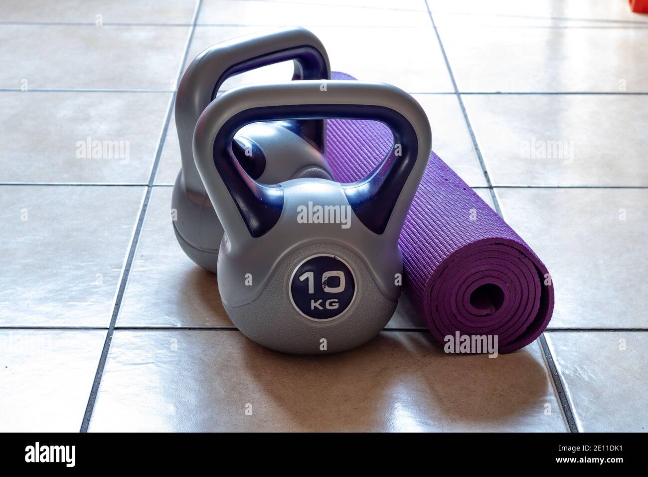 Deux poids kettlebell de 10 kg et tapis de yoga violet sur le sol Banque D'Images