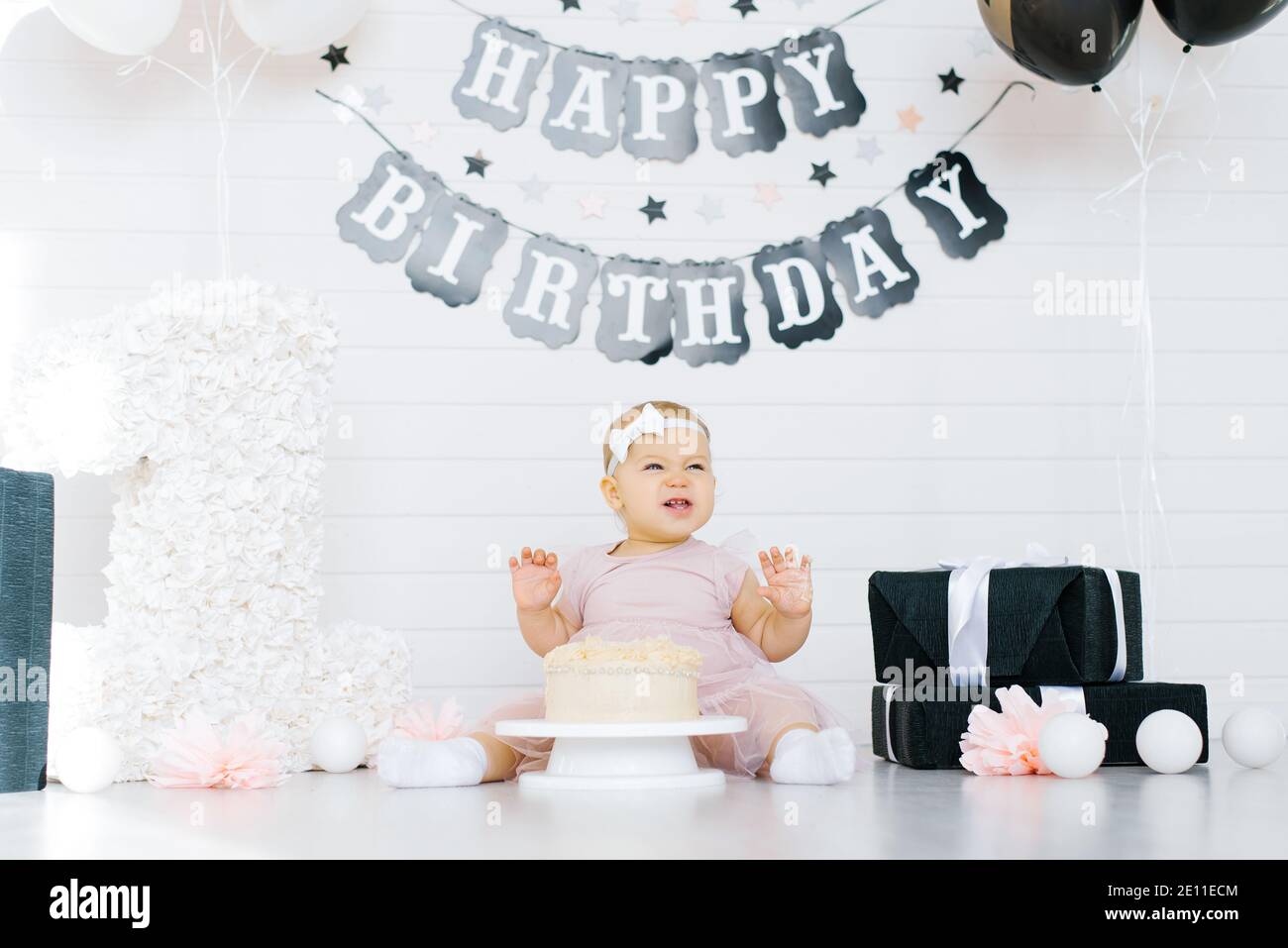 Célébration du premier anniversaire d'une petite fille. Un enfant s'assoit près d'un gâteau dans une zone de photo festive Banque D'Images