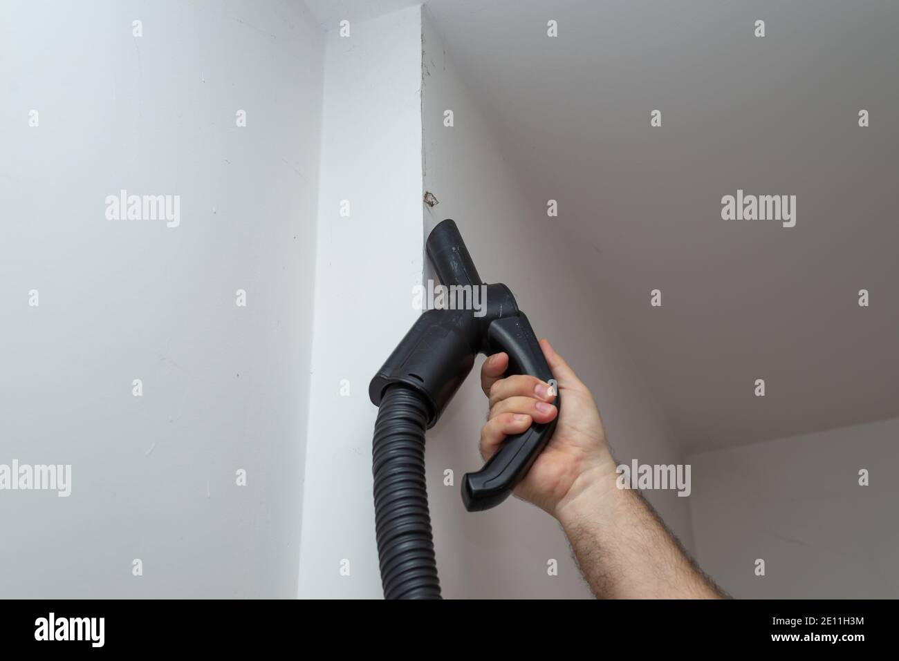 Main d'un homme tenant un aspirateur tout en passant l'aspirateur saleté sur un mur Banque D'Images