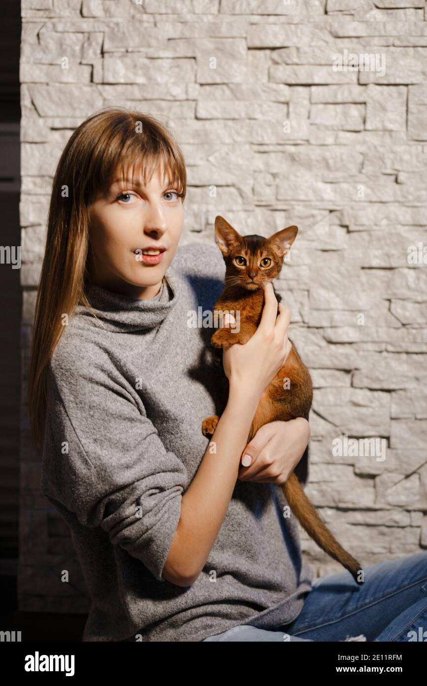 Jeune femme mignonne jouant avec un petit chat ou chaton Abyssinien à la maison contre le mur blanc Banque D'Images