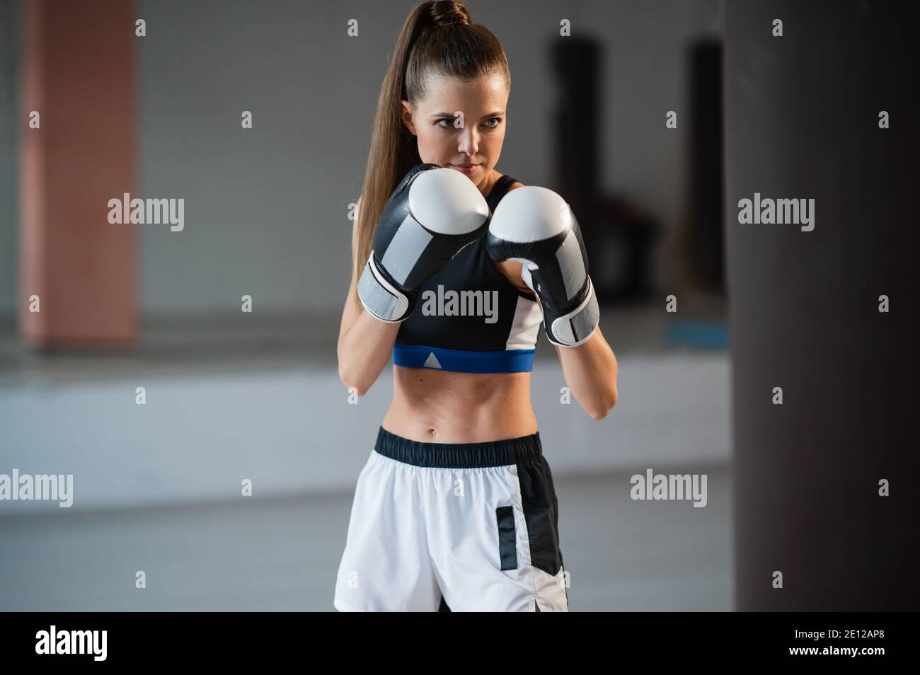 La jeune fille se prépare pour une compétition de boxe et des trains punchs sur un sac de poinçonnage dans une salle de sport spacieuse Banque D'Images