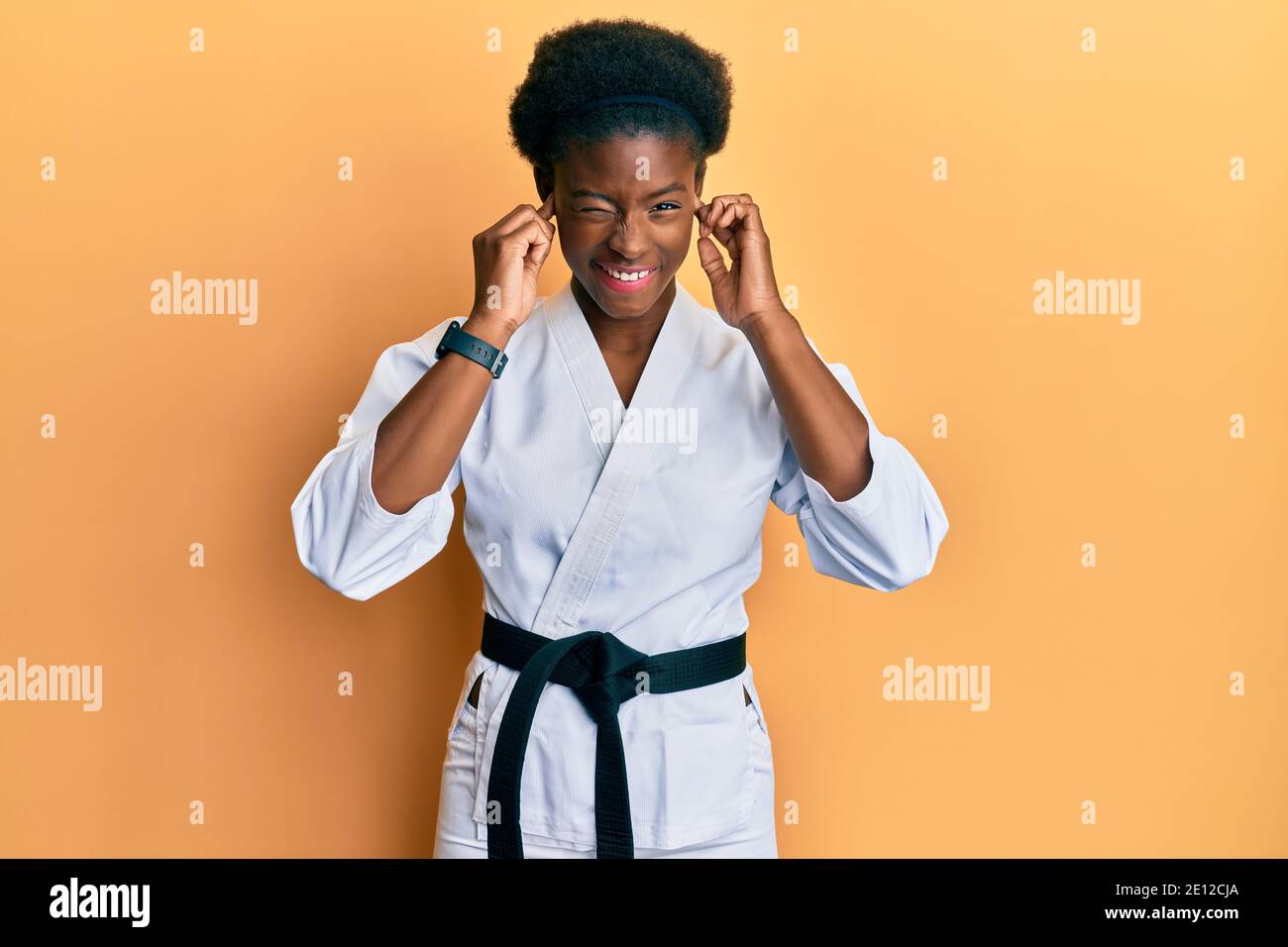 Jeune fille afro-américaine portant un kimono de karaté et une ceinture  noire couvrant les oreilles avec les doigts avec l'expression agacée pour  le bruit de la musique forte. Sourd Photo Stock -