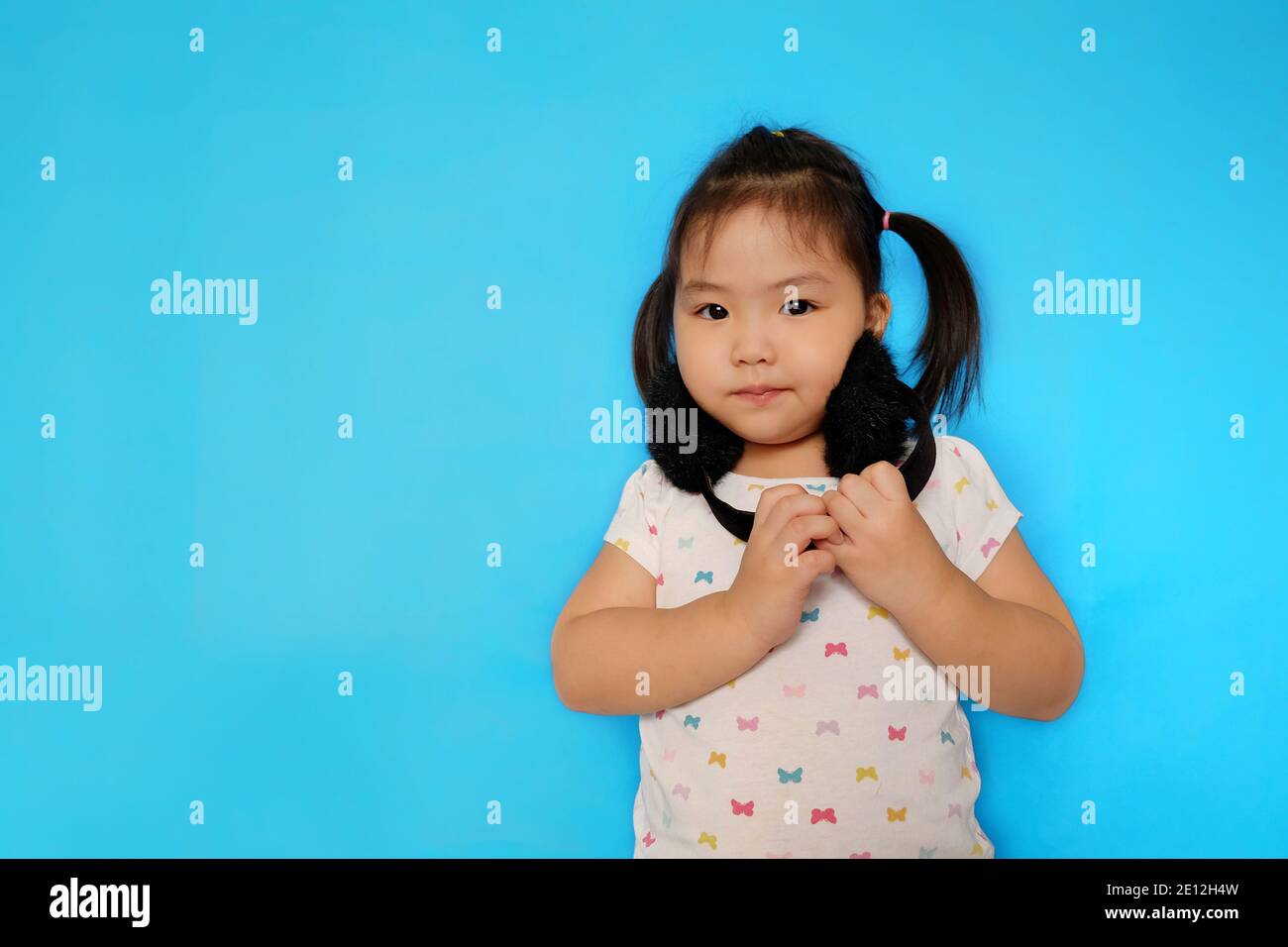 Une adorable jeune fille asiatique à l'écoute de musiques avec son casque doux noir, souriant, amusant. Fond bleu clair Uni. Banque D'Images