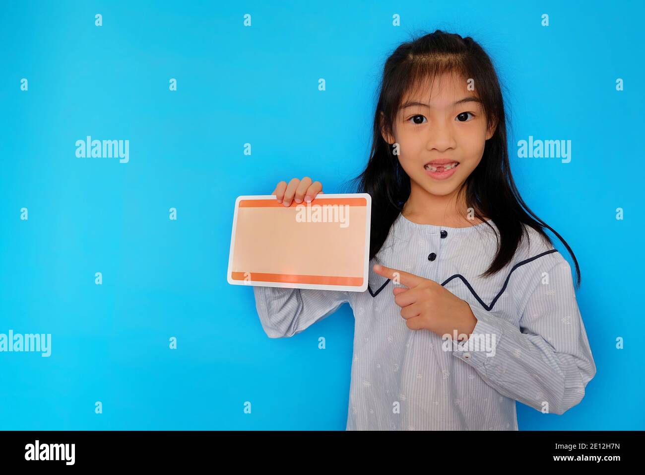 Une jeune fille asiatique mignonne debout sur un fond bleu clair Uni, tenant un morceau de papier vierge, souriant. Banque D'Images
