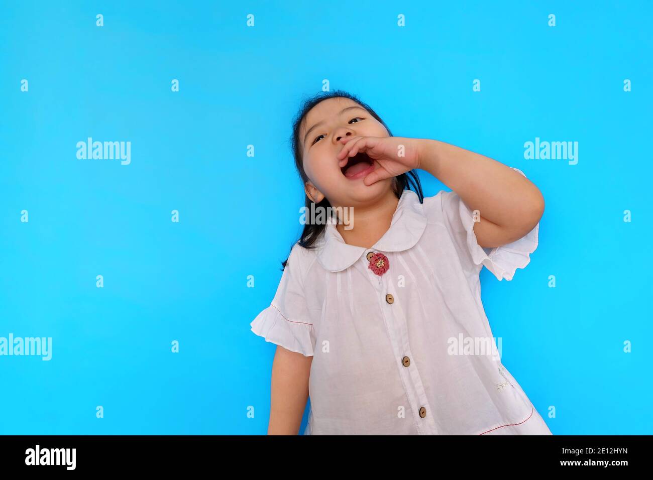 Une jeune fille asiatique mignonne se sentant excitante, criant du haut de ses poumons avec sa bouche large ouverte et une paume près de sa bouche. Fond bleu clair Uni Banque D'Images