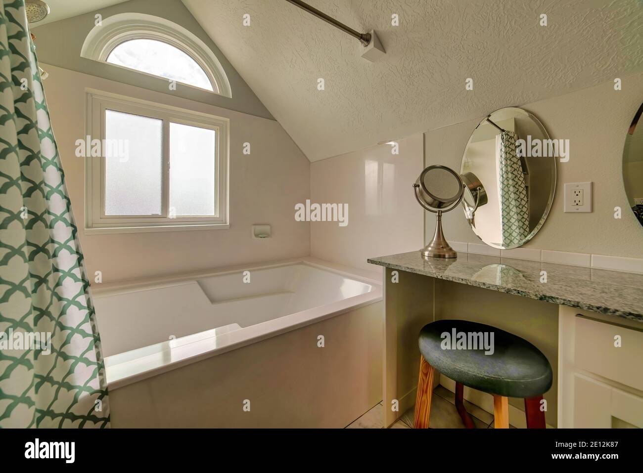 Meuble-lavabo en marbre avec tabouret et miroir ovale à côté baignoire dans la salle de bains Banque D'Images