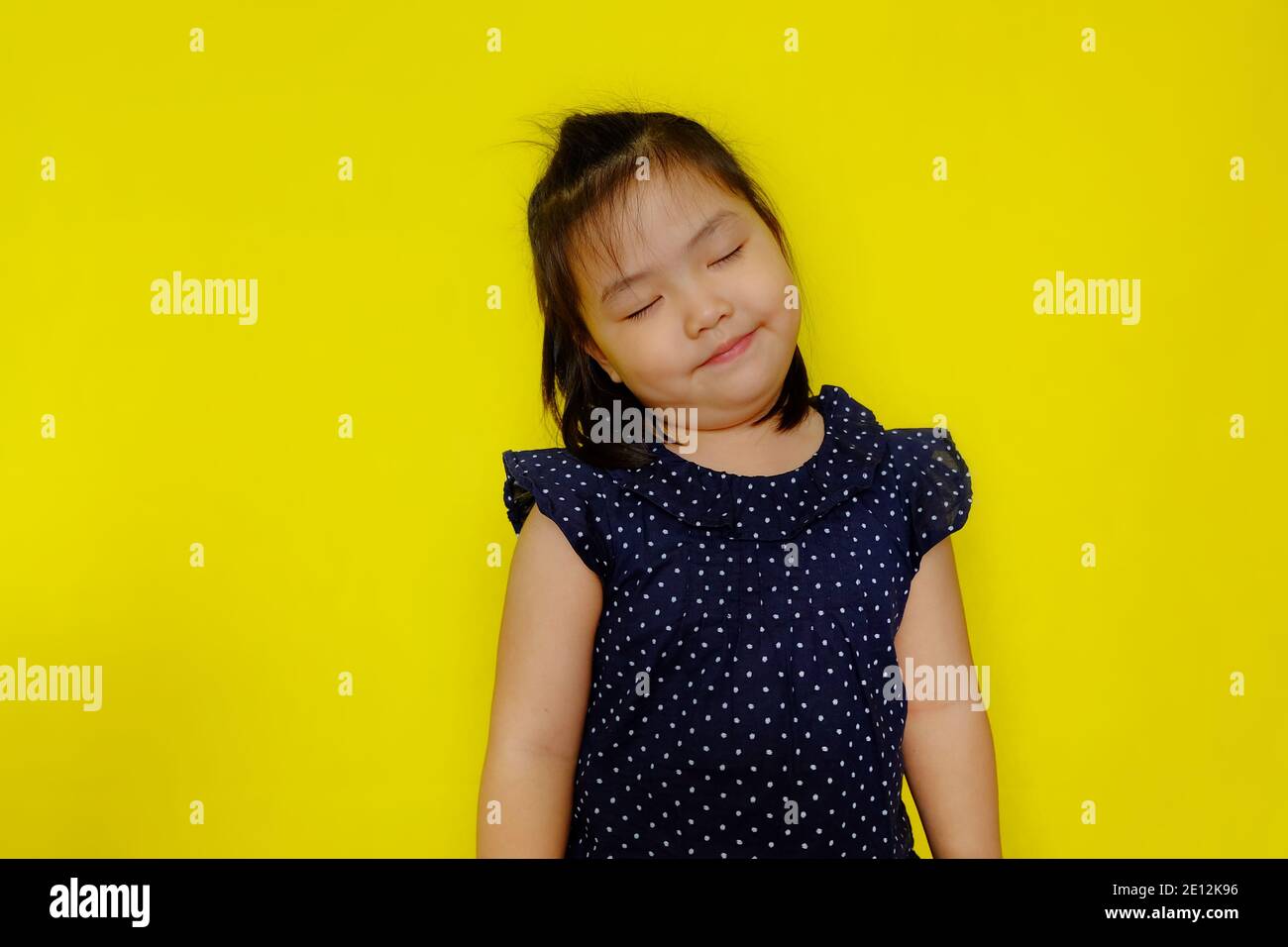 Une jolie jeune fille asiatique rêvant de jour, souriant avec ses yeux proches et une pensée heureuse. Arrière-plan jaune vif. Banque D'Images