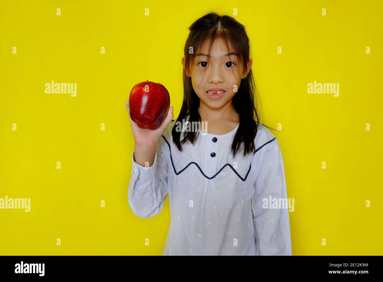 Une jolie jeune fille asiatique tenant une pomme, se préparer à la manger pour le petit déjeuner. Arrière-plan jaune vif. Banque D'Images