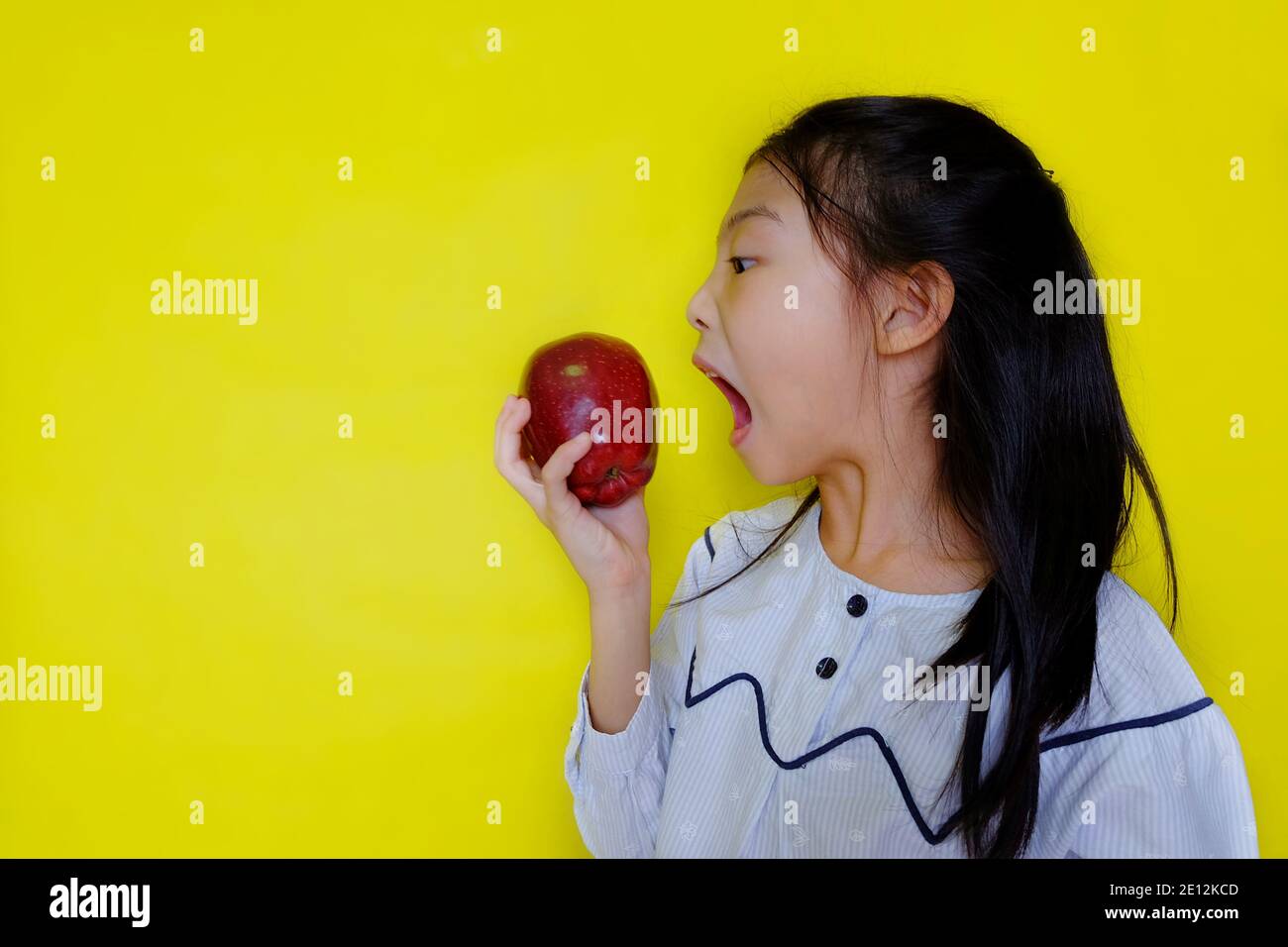 Une jolie jeune fille asiatique attrapant une pomme rouge, essayant de prendre une morsure. Arrière-plan jaune vif. Banque D'Images