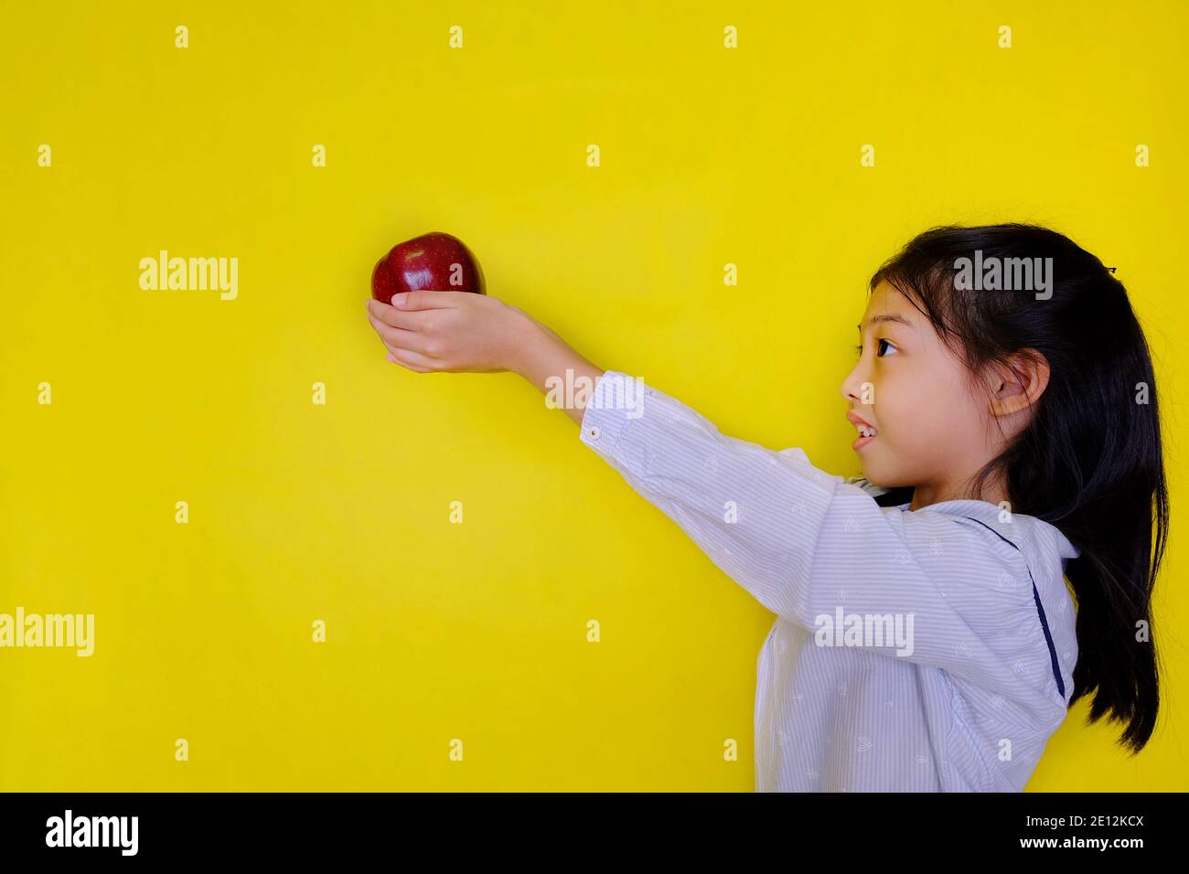 Une jolie jeune fille asiatique à l'école, donnant une pomme rouge à son professeur comme cadeau, souriant. Arrière-plan jaune vif. Banque D'Images