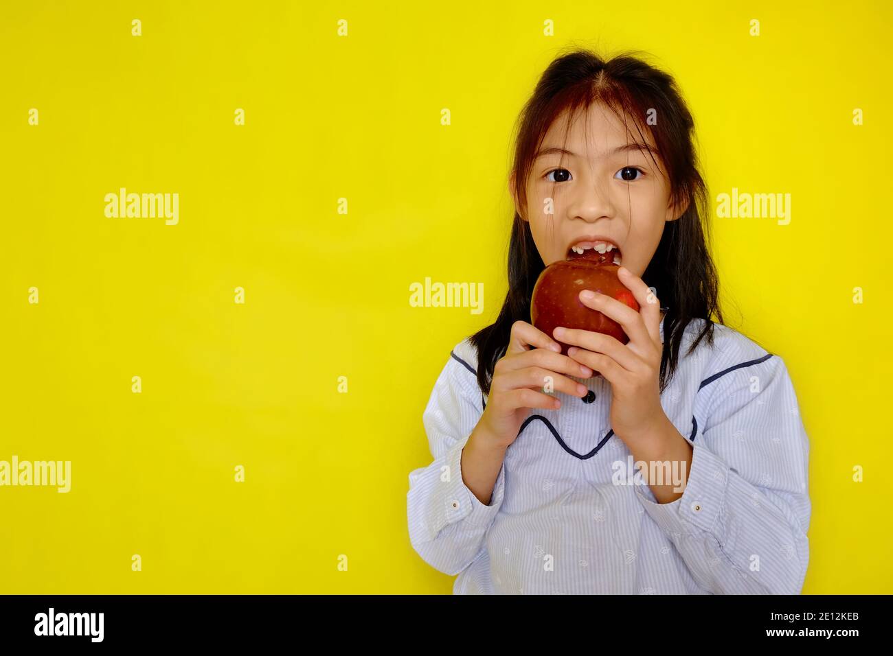 Une jolie jeune fille asiatique attrapant une pomme rouge, essayant de prendre une morsure. Arrière-plan jaune vif. Banque D'Images