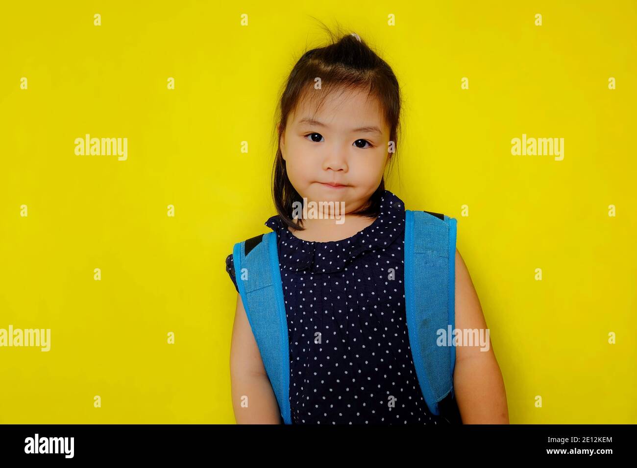 Une jeune fille asiatique mignonne porte un grand sac à dos bleu sur son dos, attendant que le bus scolaire va à l'école le matin. Fond de couleur jaune vif Banque D'Images