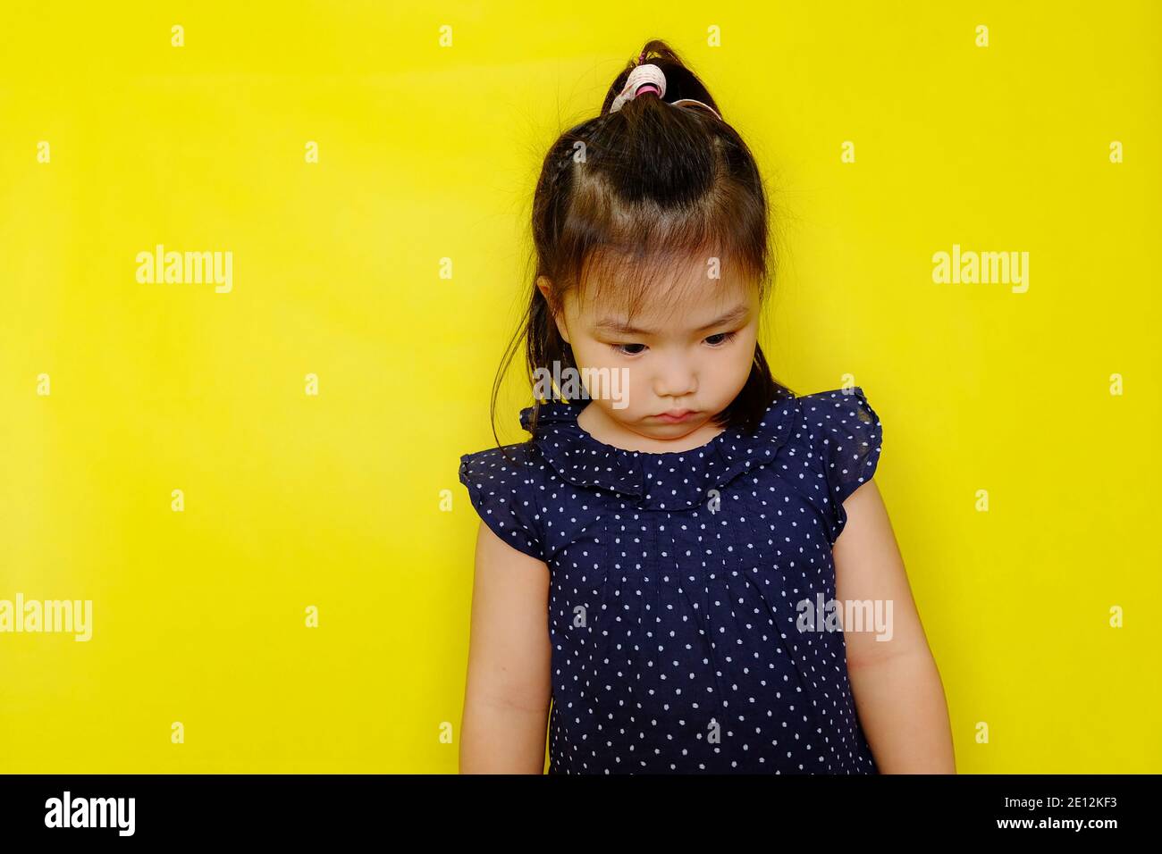 Une jolie jeune fille asiatique debout seule se sentant bouleversée, frustrée, et déçue, regardant vers le bas, pensant. Arrière-plan jaune vif. Banque D'Images