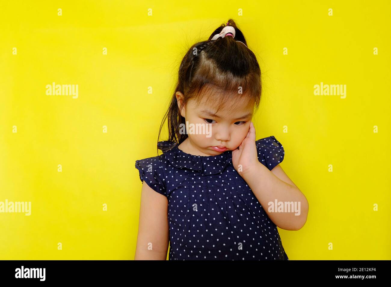 Une jolie jeune fille asiatique debout seule se sentant bouleversée, frustrée, et déçue, regardant vers le bas, pensant. Arrière-plan jaune vif. Banque D'Images
