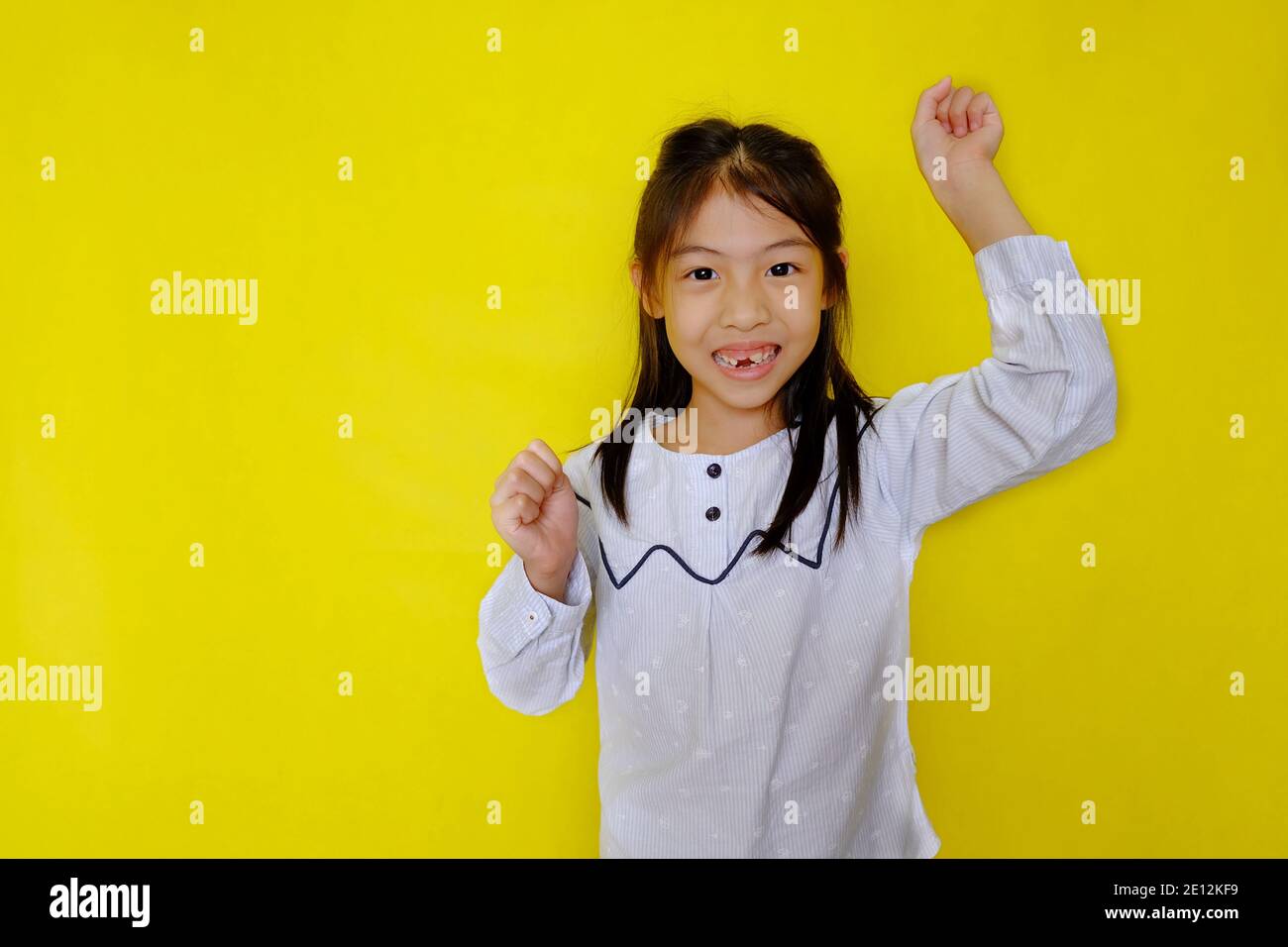 Une mignonne jeune fille asiatique intelligente et excitant sa main pour répondre à une question dans une salle de classe. Arrière-plan jaune vif. Banque D'Images