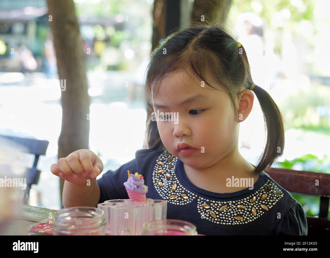 Une jeune fille asiatique mignonne se concentre sur la décoration de sa crème glacée en forme de cône jouer la pâte, ajoutant des saupoudrées colorées comme garniture. Banque D'Images