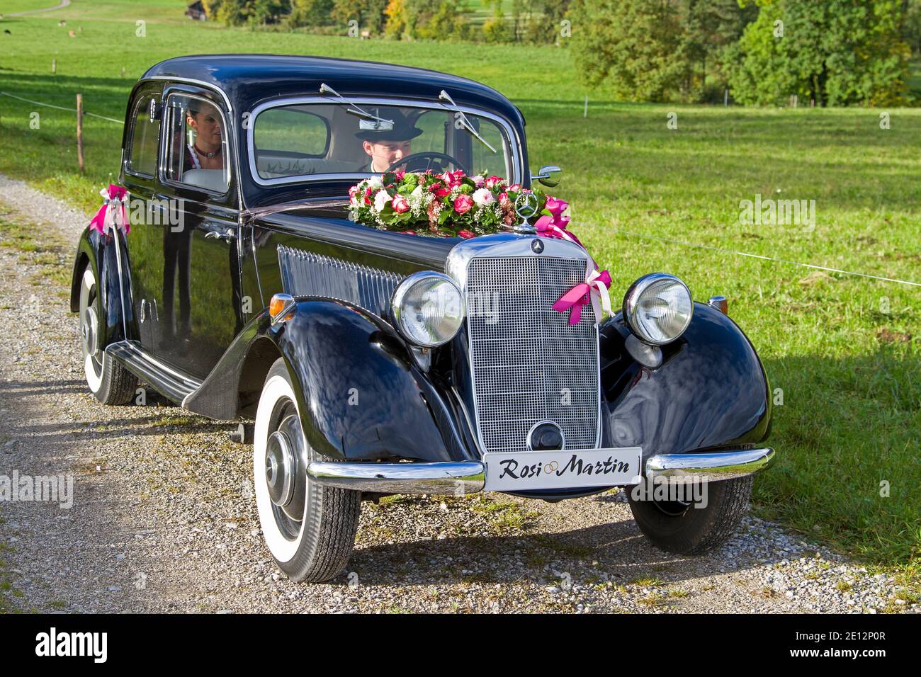 Vieille Mercedes-Benz noire décorée de fleurs apporte le Jeune Couple de mariage à l'Église Banque D'Images