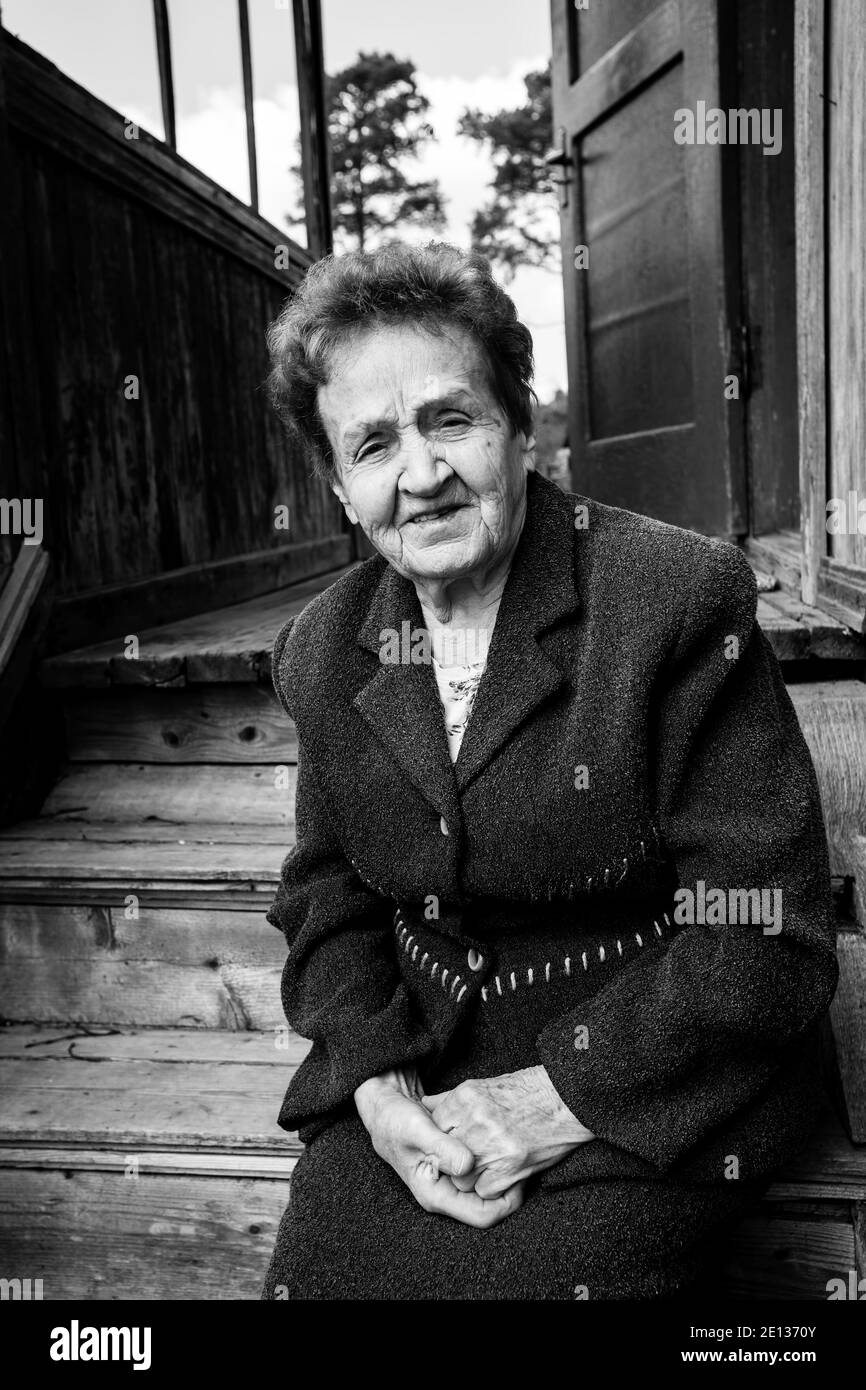 Vieille femme assise sur le porche de la maison. Photo en noir et blanc. Banque D'Images