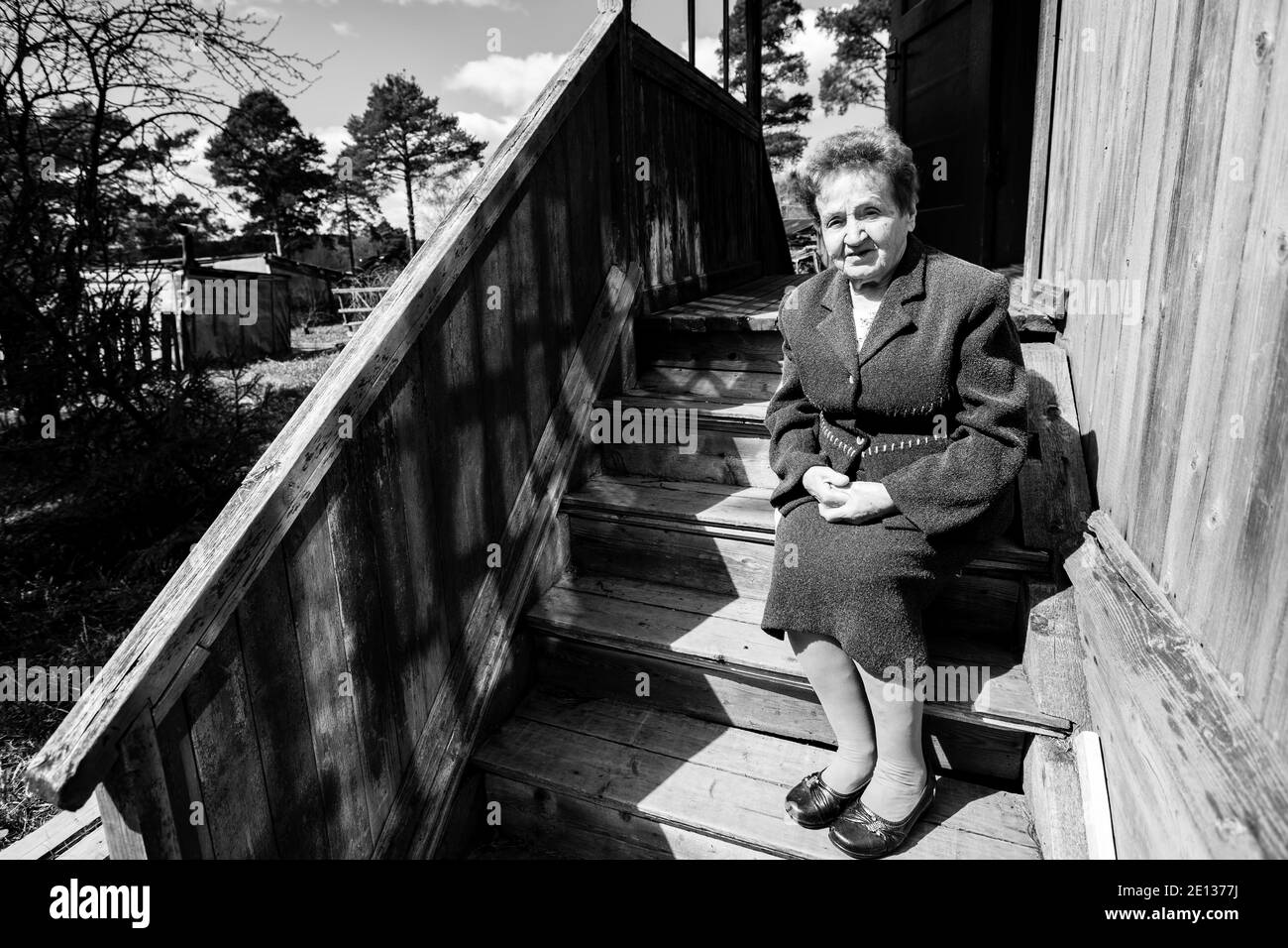 Vieille femme assise sur le porche d'une maison de village. Photo en noir et blanc. Banque D'Images