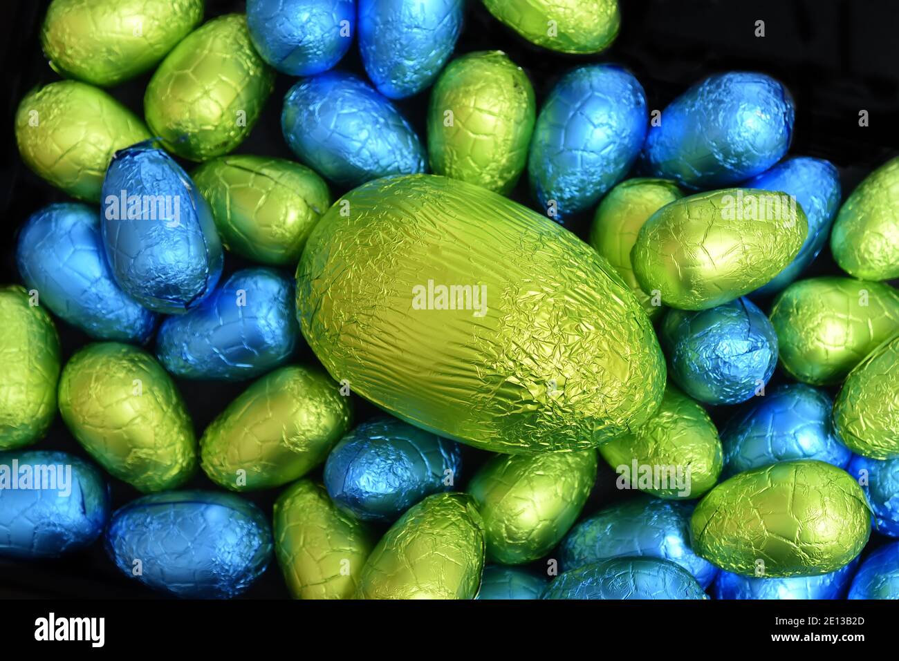 Pile de plusieurs couleurs et de différentes tailles de papier d'aluminium coloré chocolat oeufs de pâques en bleu, jaune et vert lime avec un gros oeuf vert. Banque D'Images