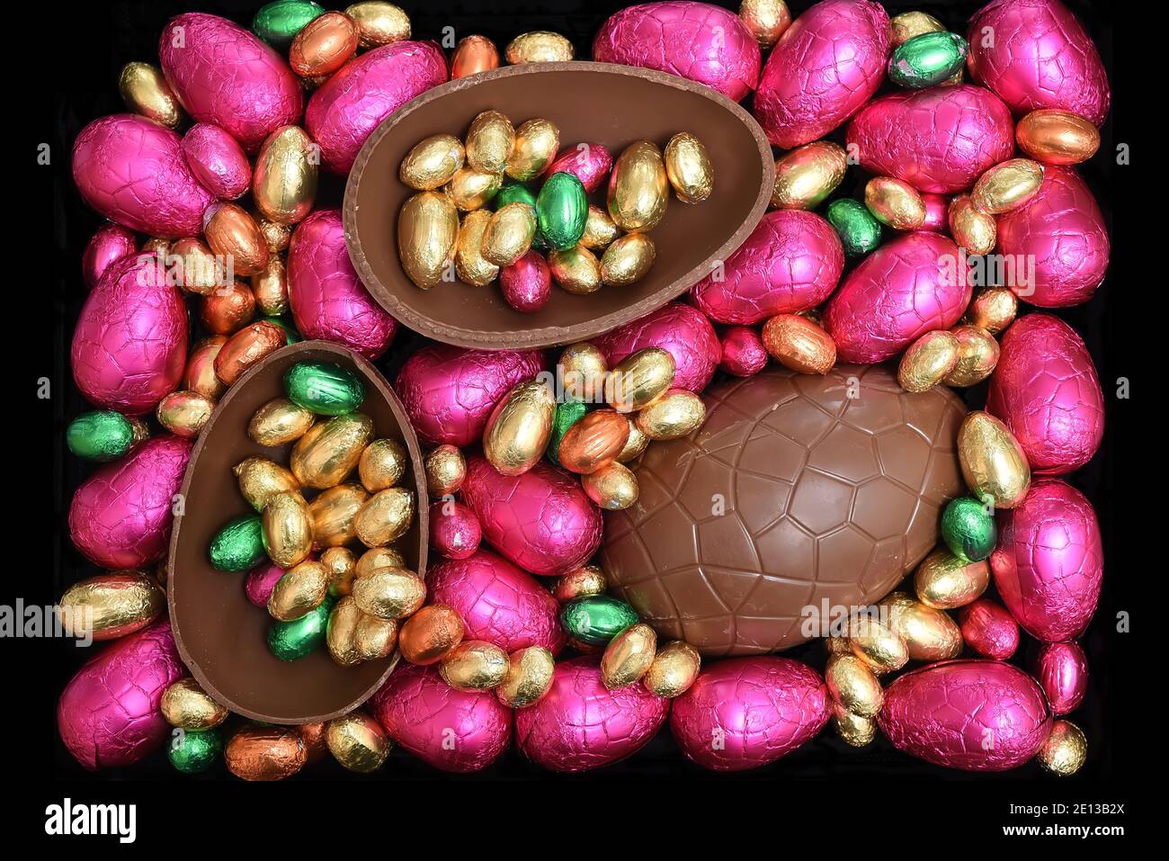 Pile ou groupe de plusieurs couleurs et différentes tailles d'oeufs de pâques au chocolat enveloppés d'une feuille colorée dans le rose, le rouge, l'or et le vert lime avec deux moitiés o Banque D'Images
