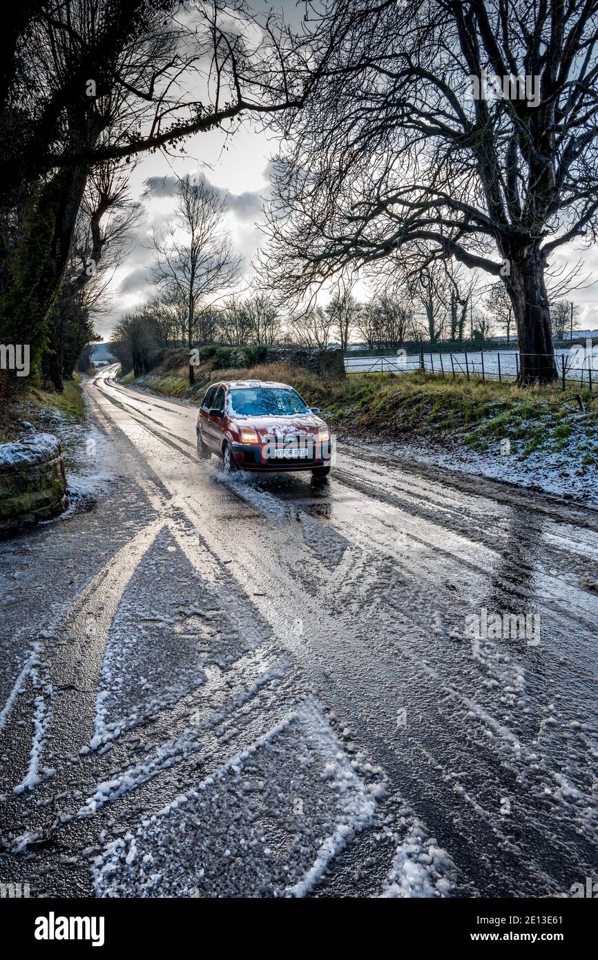 Voiture roulant le long d'une route de campagne dégelée de neige. Banque D'Images