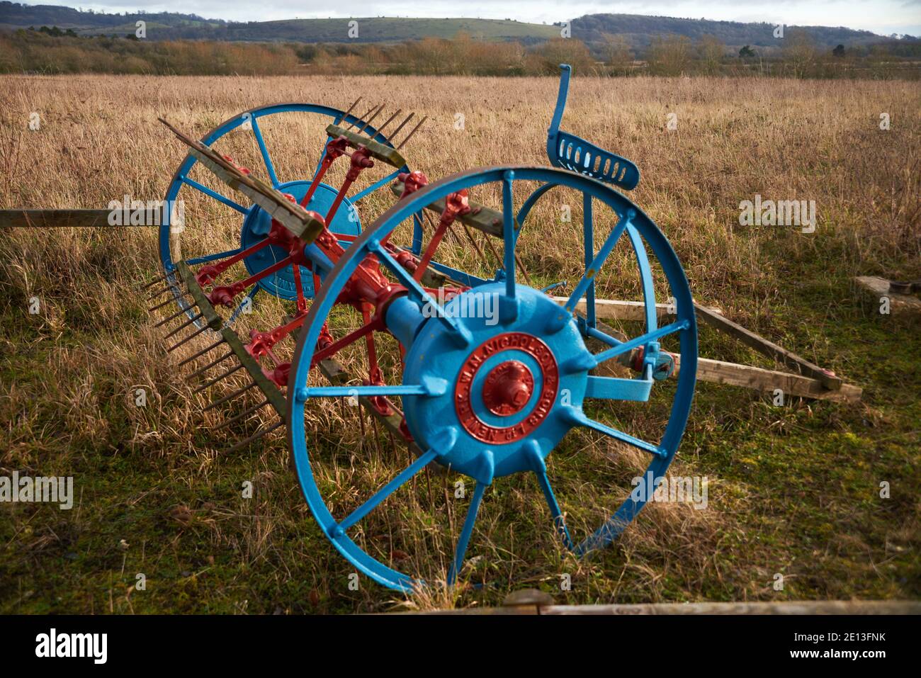 Vieux matériel agricole dans le champ, faneuse tirée par des chevaux des années 1800 peinte en rouge et bleu Banque D'Images