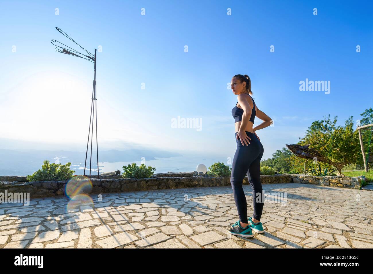 Jeune femme se préparant pour ses exercices matinaux debout à l'extérieur le jardin sur un patio en pierre dans sportswear dans un concept de santé et de forme physique Banque D'Images