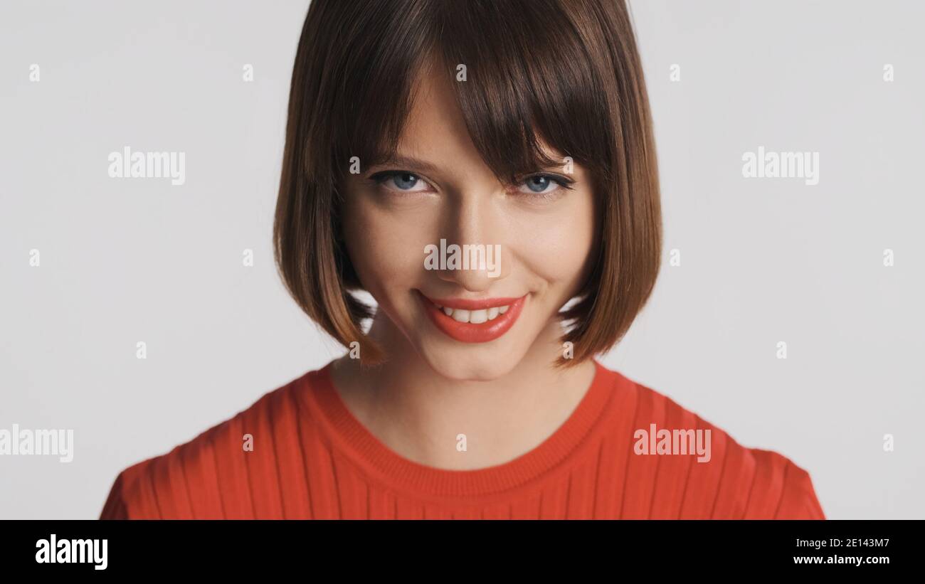 Jolie fille brune avec des cheveux de bob et des lèvres rouges regardant slyly dans l'appareil photo et souriant sur fond blanc. Banque D'Images