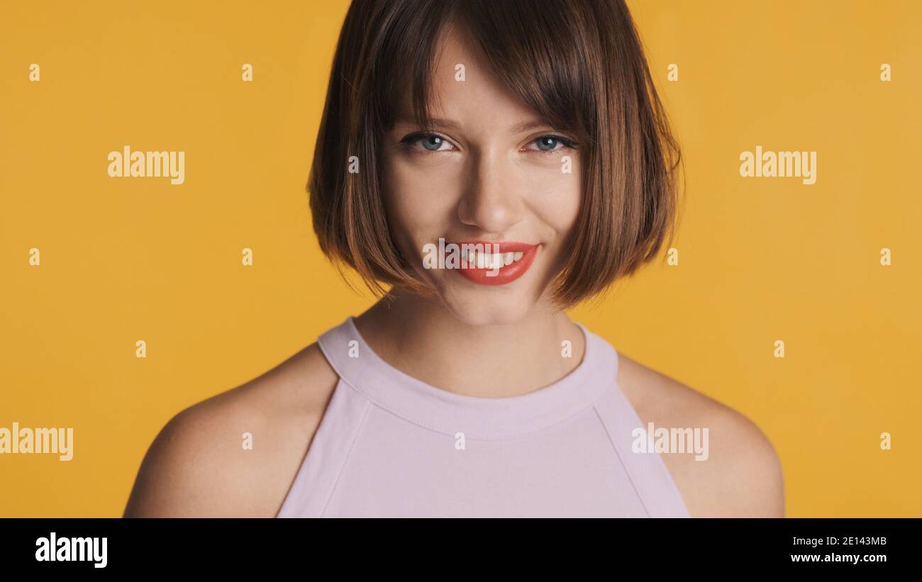 Charmante fille brune avec des cheveux de bob et des lèvres rouges heureusement regarder dans l'appareil photo sur un arrière-plan coloré Banque D'Images