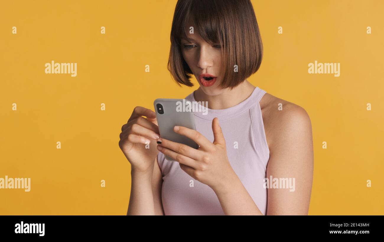 Jolie surprise brunette fille discutant avec des amis dans le réseau social look étonné isolé sur fond jaune. Wow expression de visage Banque D'Images