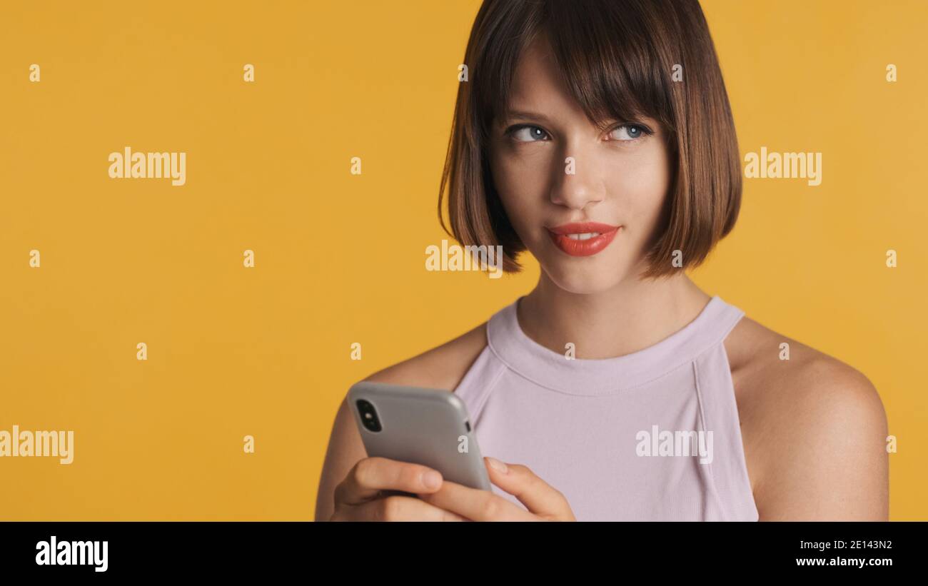 Jolie petite fille de brunes charmante avec bob Hair en train de bavarder avec petit ami utilisant un smartphone isolé sur fond coloré Banque D'Images