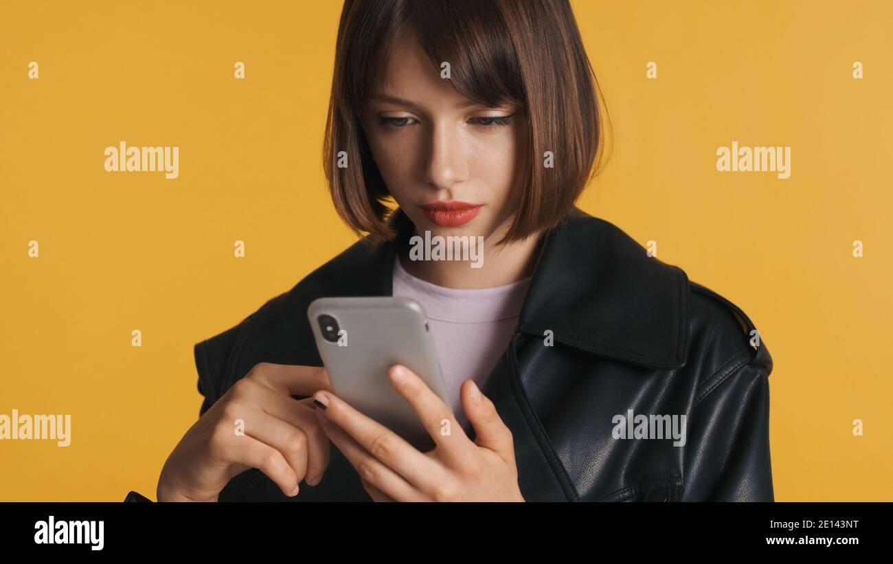 Belle fille de brunette avec bob cheveux en utilisant le smartphone sur l'appareil photo isolé sur fond jaune Banque D'Images