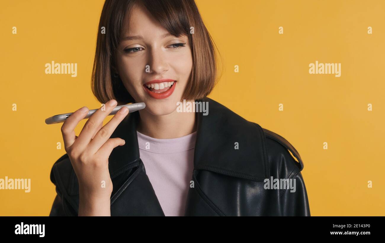 Jolie fille brunette avec bob cheveux enregistrement message vocal à meilleur ami sur smartphone isolé sur fond jaune Banque D'Images