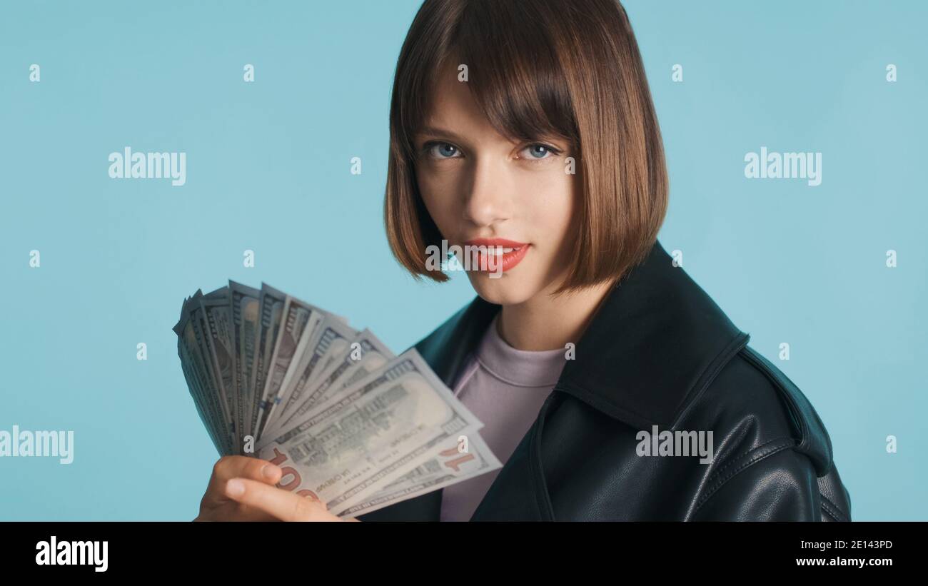 Belle fille brune avec cheveux de bob et lèvres rouges tenant argent à l'image de la caméra sur fond bleu Banque D'Images