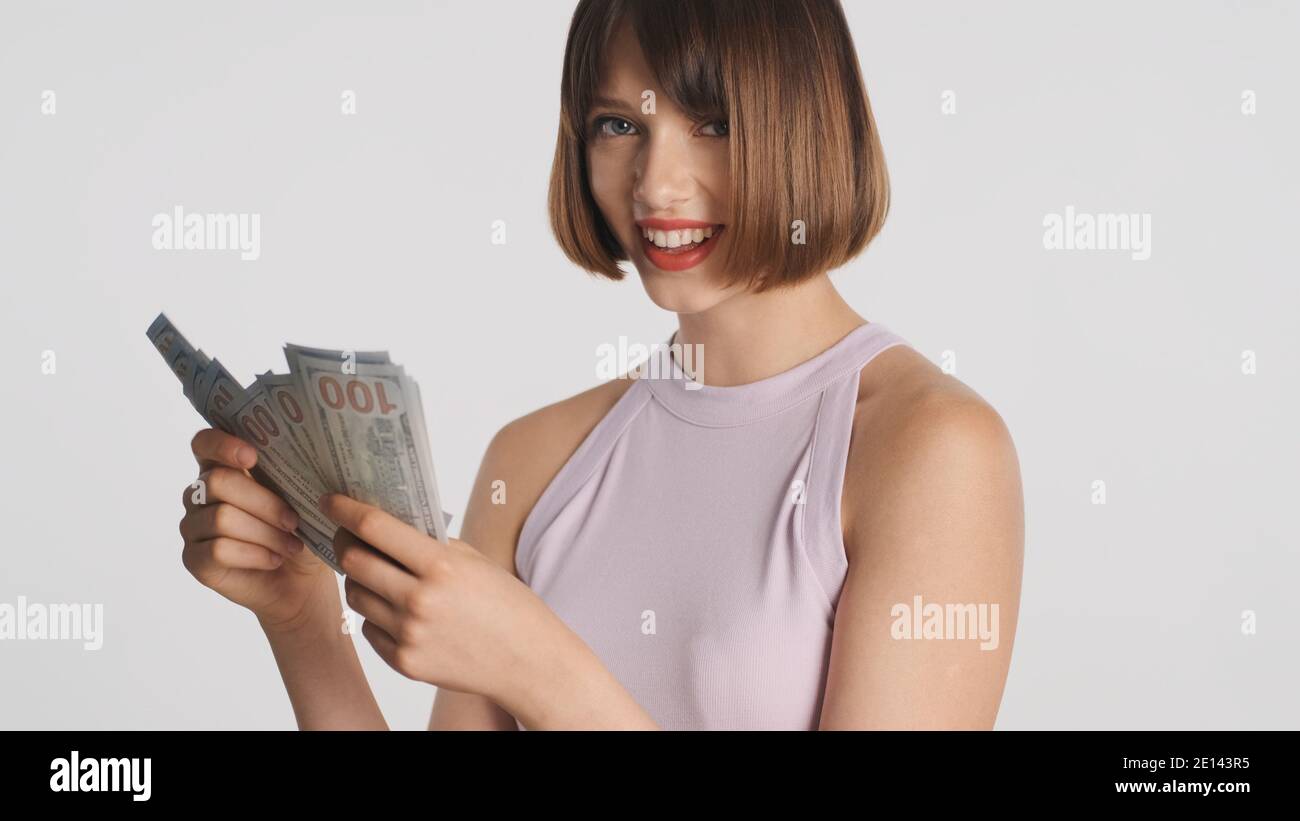 Portrait de gaie brune fille heureux comptant l'argent sur l'appareil photo sur fond blanc. Insouciante fille Banque D'Images