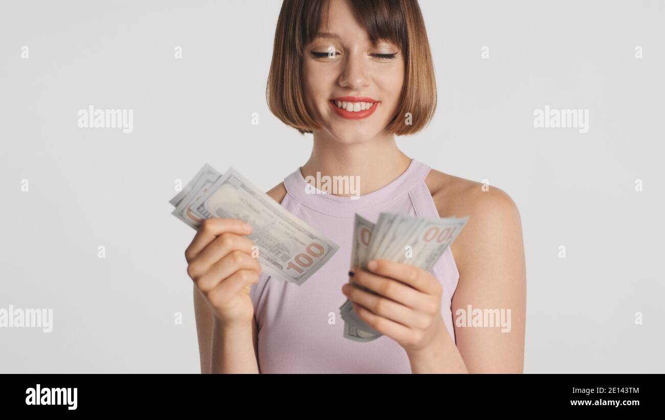 Jolie fille de brunette gaie avec bob les cheveux semblent heureux compter argent sur caméra isolée sur fond blanc Banque D'Images