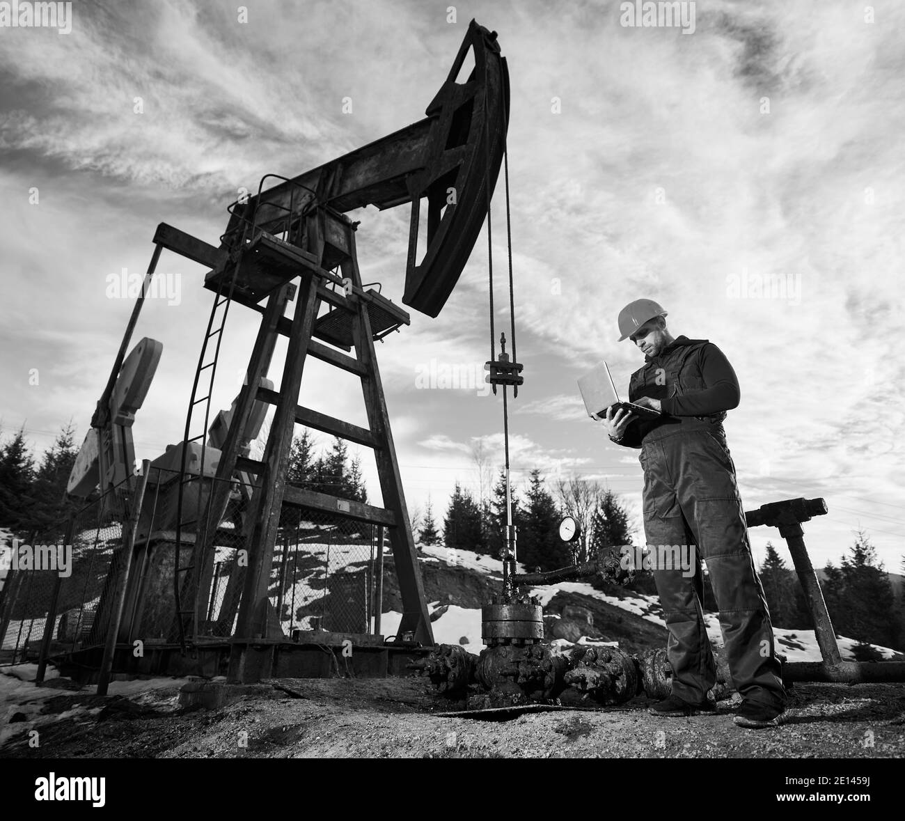 Homme utilisant un ordinateur portable pour contrôler le travail du cric de la pompe à pétrole. Opérateur à proximité de l'unité de pompage d'huile. Concept de l'industrie pétrolière et de l'extraction de pétrole. Image en noir et blanc Banque D'Images