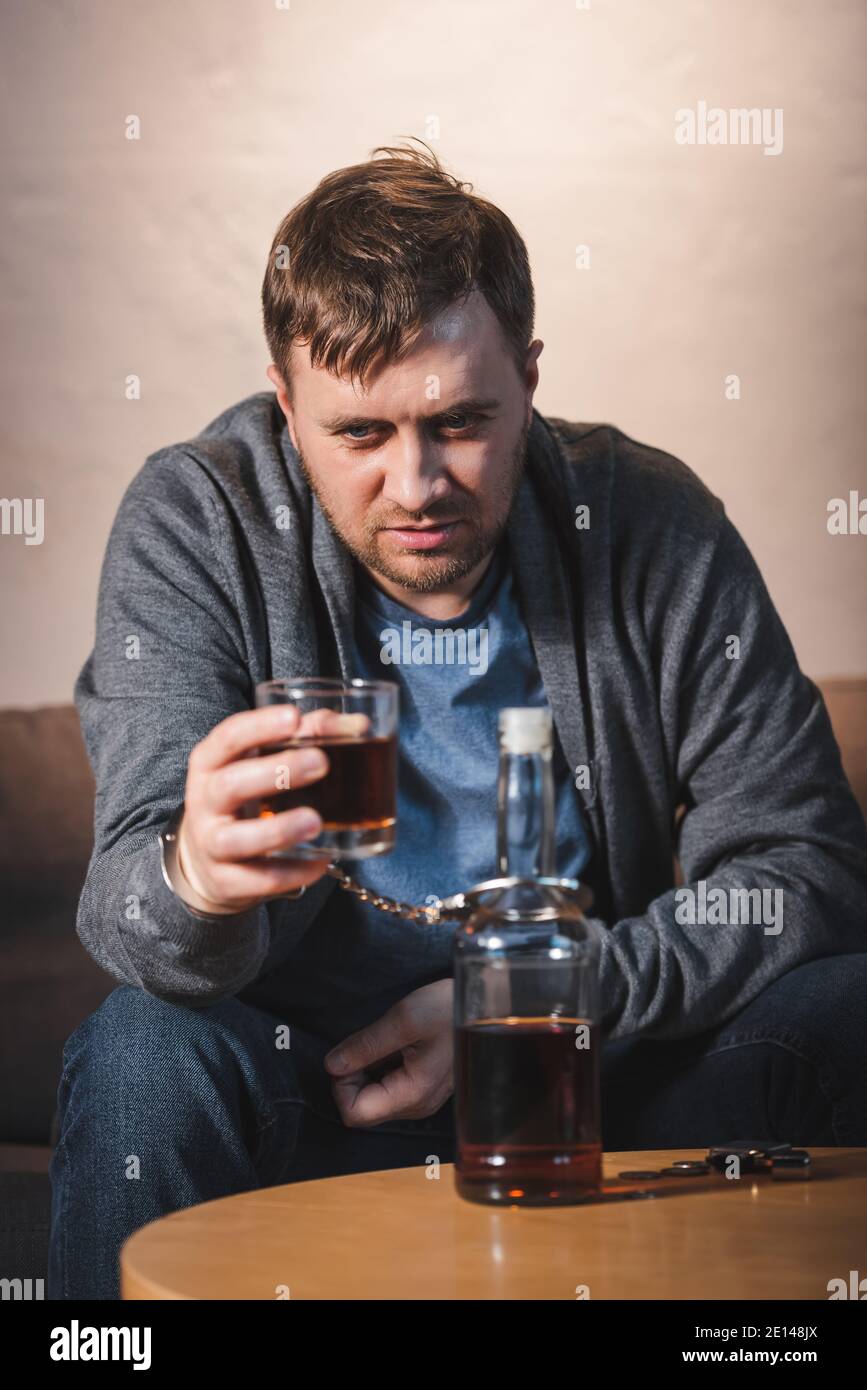 homme ivre, menotté à une bouteille d'alcool, tenant un verre de whisky,  flou de premier plan Photo Stock - Alamy